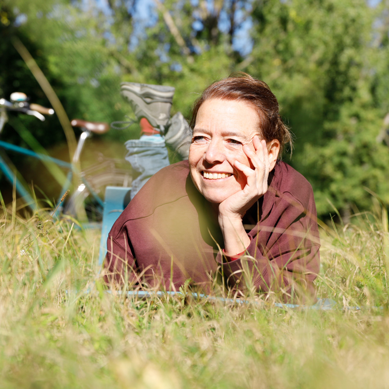 Regine Meier im Gras liegend, Hand aufgestützt, Fahrrad im Hintergrund