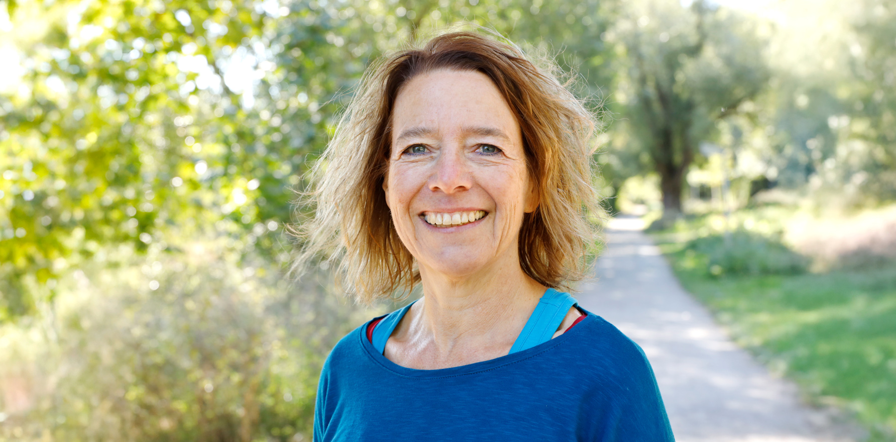 Portraitfoto von Regine Meier, im Hintergrund Bäume und ein Weg