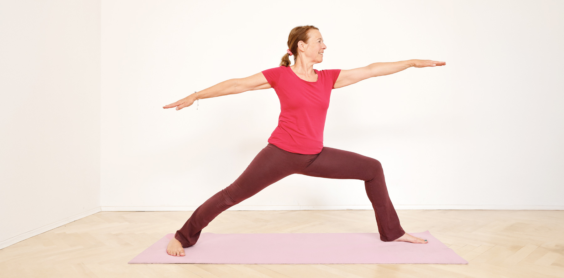 Frau mit Zopf in Yoga-Stellung 'der Krieger' in hellem Raum